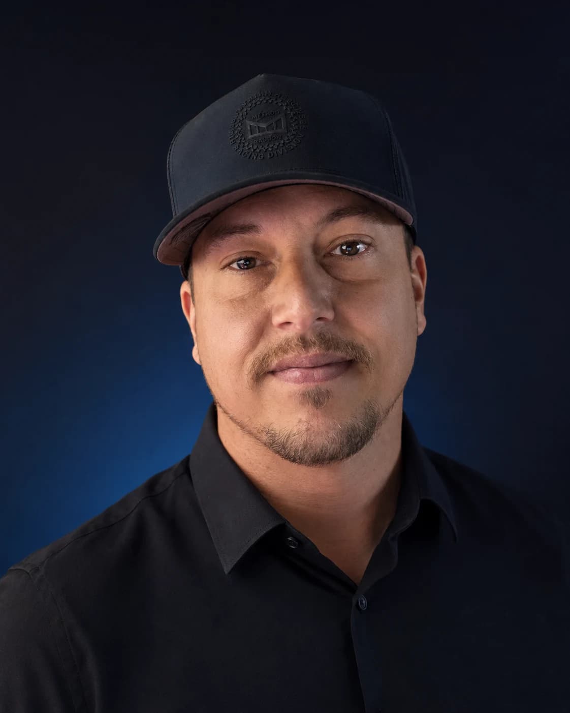 John C. Hockinson Jr. in a black shirt and cap against a deep blue backdrop